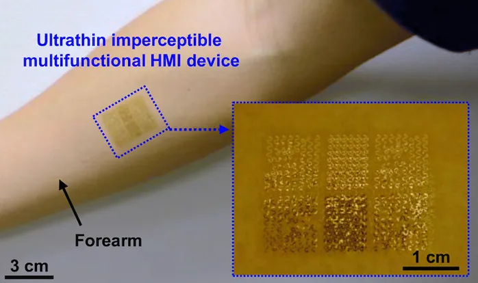 An ultrathin, imperceptible multifunctional human–machine-interface device laminated onto a forearm, with a magnified inset revealing its fine gold sensor and electrode array.