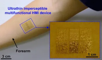 An ultrathin, imperceptible multifunctional human–machine-interface device laminated onto a forearm, with a magnified inset revealing its fine gold sensor and electrode array.